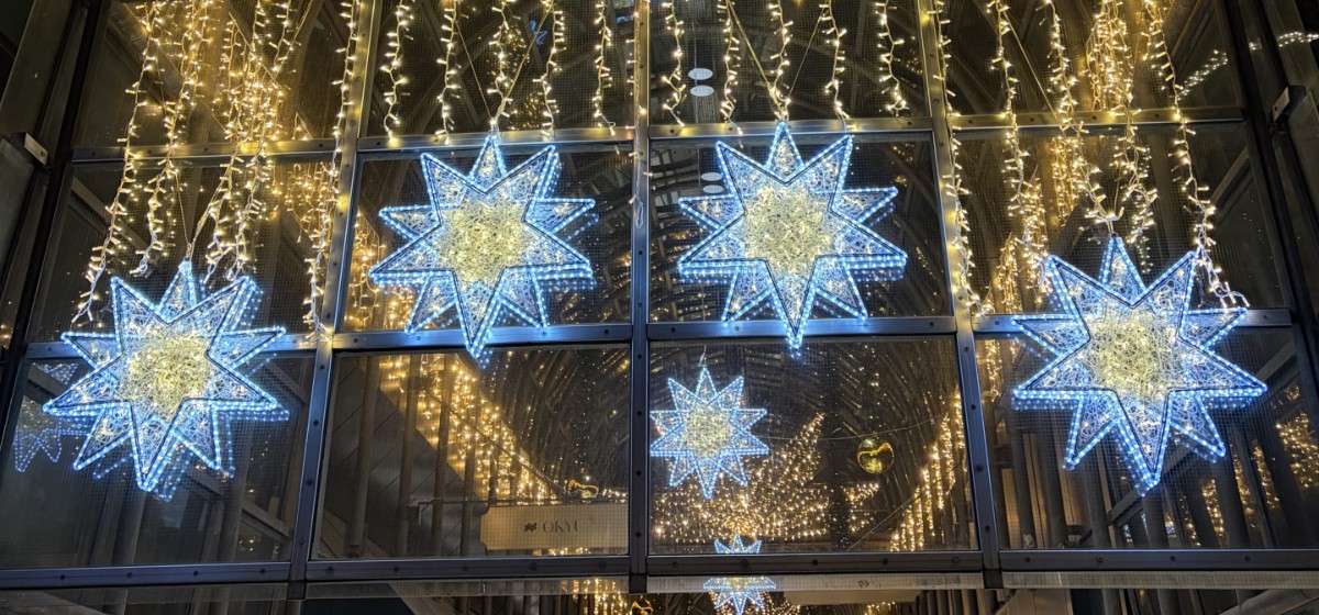 Jahresrückblick 2025 – beleuchtete Sternmotive hängen vor einer Glasfassade, umgeben von Lichterketten in warmem und kühlem Licht.