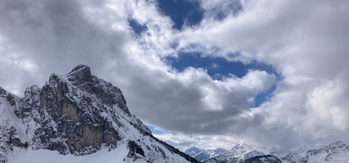 An der Spitze ist es einsam – schneebedeckter Alpenberg mit markanter Felswand, im Hintergrund weitere Gipfel unter wechselhaftem Wolkenhimmel.